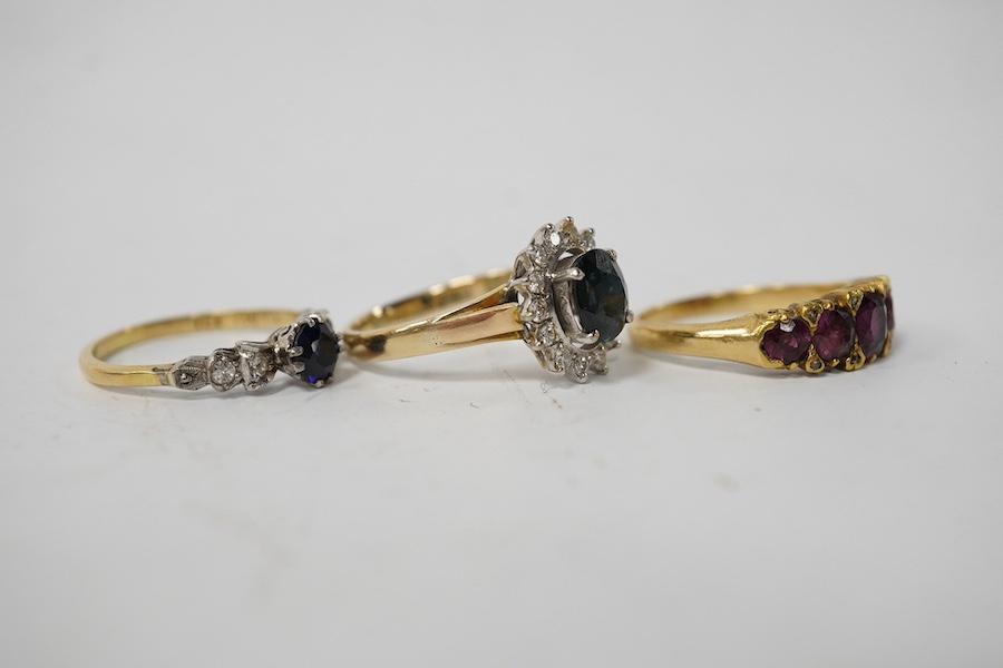 A group of three rings, comprising: a sapphire and diamond cluster ring, size M1/2, stamped 14K and 585; a five-stone ring set with cushion-shaped garnets and rose-cut diamonds, size L; and a synthetic sapphire and simul